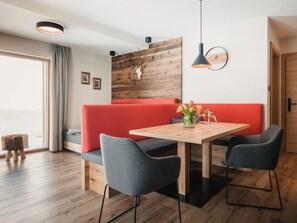 Un espace repas moderne avec une table en bois, deux chaises grises, un banc rouge et un mur en bois orné d’un motif représentant un crâne.