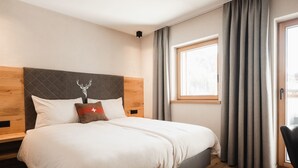 A modern hotel room with a large bed, wooden headboard, a window with curtains, and a wooden floor. - Avero Lodge by MEIN SAMNAUN – MOUNTAIN HOMES, (Samnaun-Compatsch) by Interhome (Samnaun)
