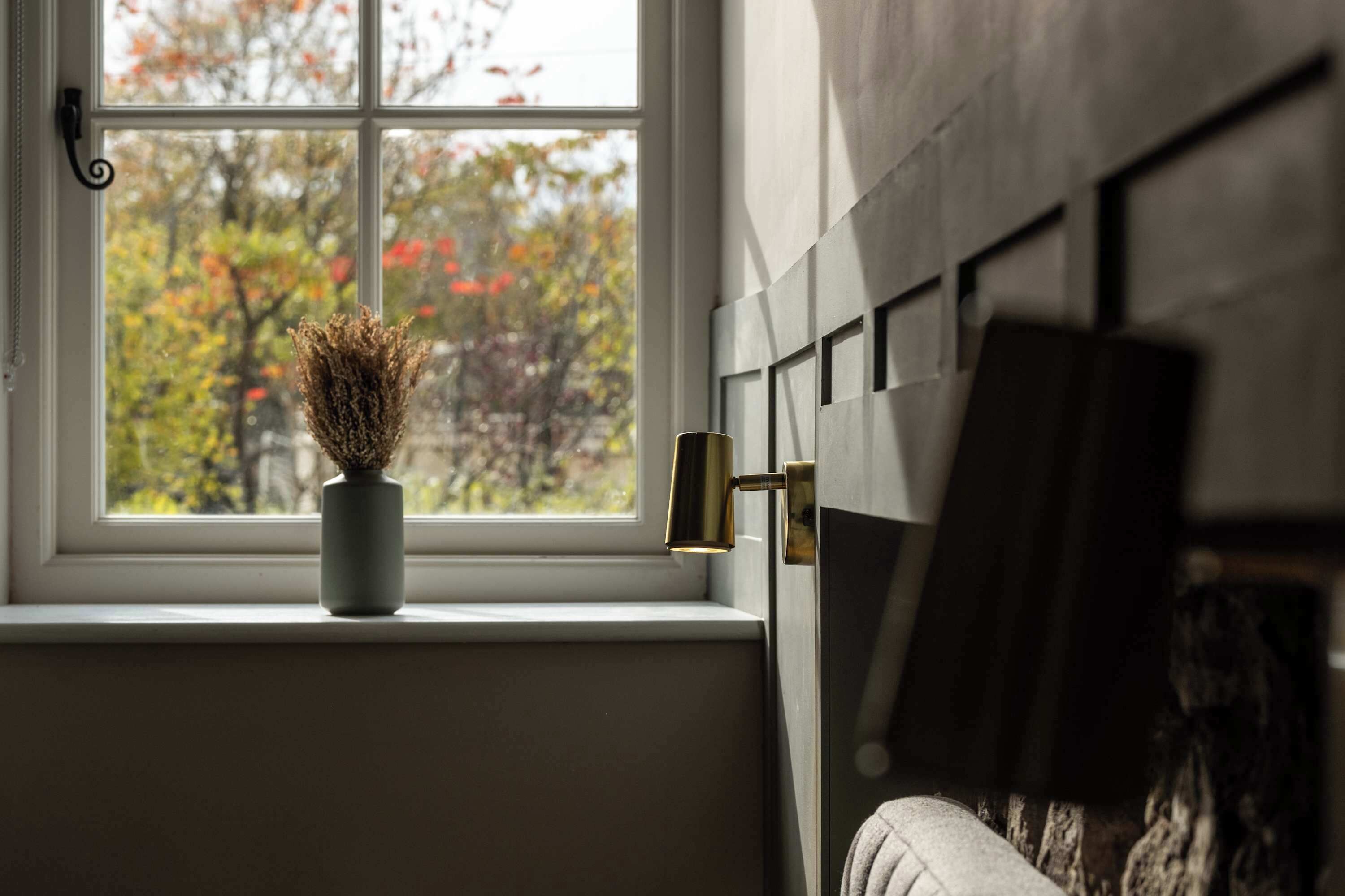 Ein Fenster mit Blick auf Bäume, eine Vase mit getrockneten Pflanzen und eine Tür mit Messinggriff.