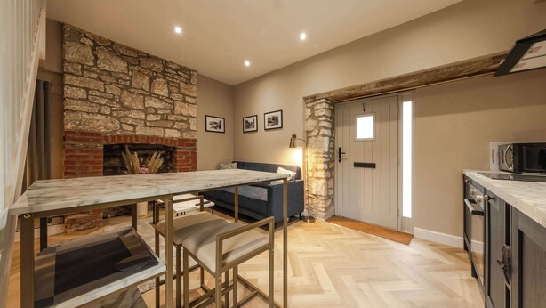 A kitchen with a stone wall, a fireplace, a dining table with chairs, a sofa, and a door with a window.
