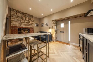 Eine Küche mit Steinwand, Kamin, Esstisch mit Stühlen, einer Couch und einer Tür mit Fenster.