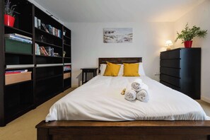 Ein ordentlich eingerichtetes Schlafzimmer mit einem großen Bett, einem Bücherregal, einer Kommode und einem Bild an der Wand.