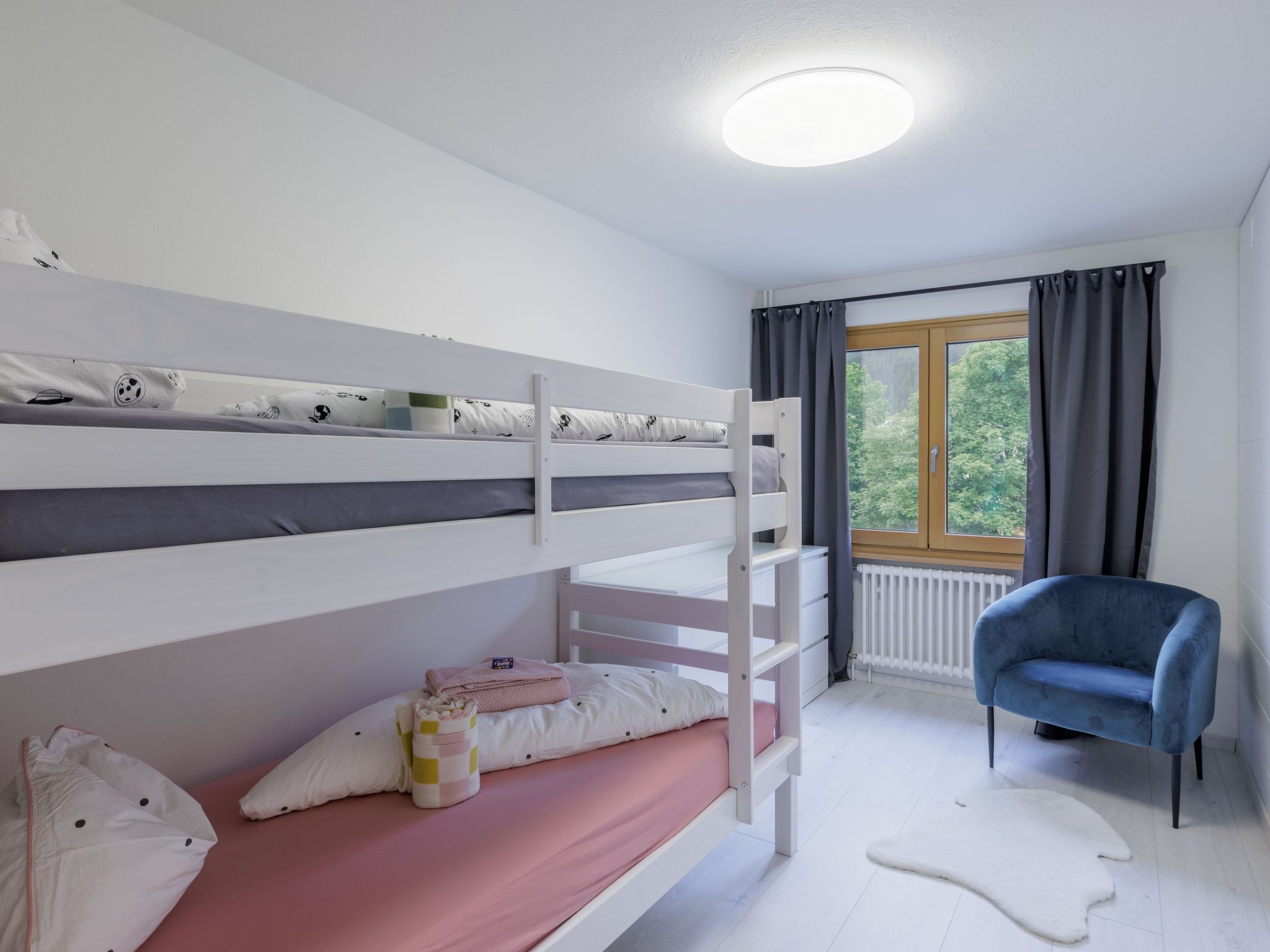Ein Schlafzimmer mit Etagenbetten, einem Fenster, einem Stuhl und einer Heizung.