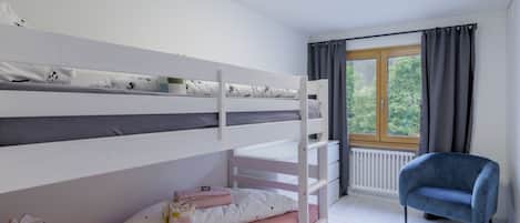 A bunk bed room with a window, a chair, and a radiator.
