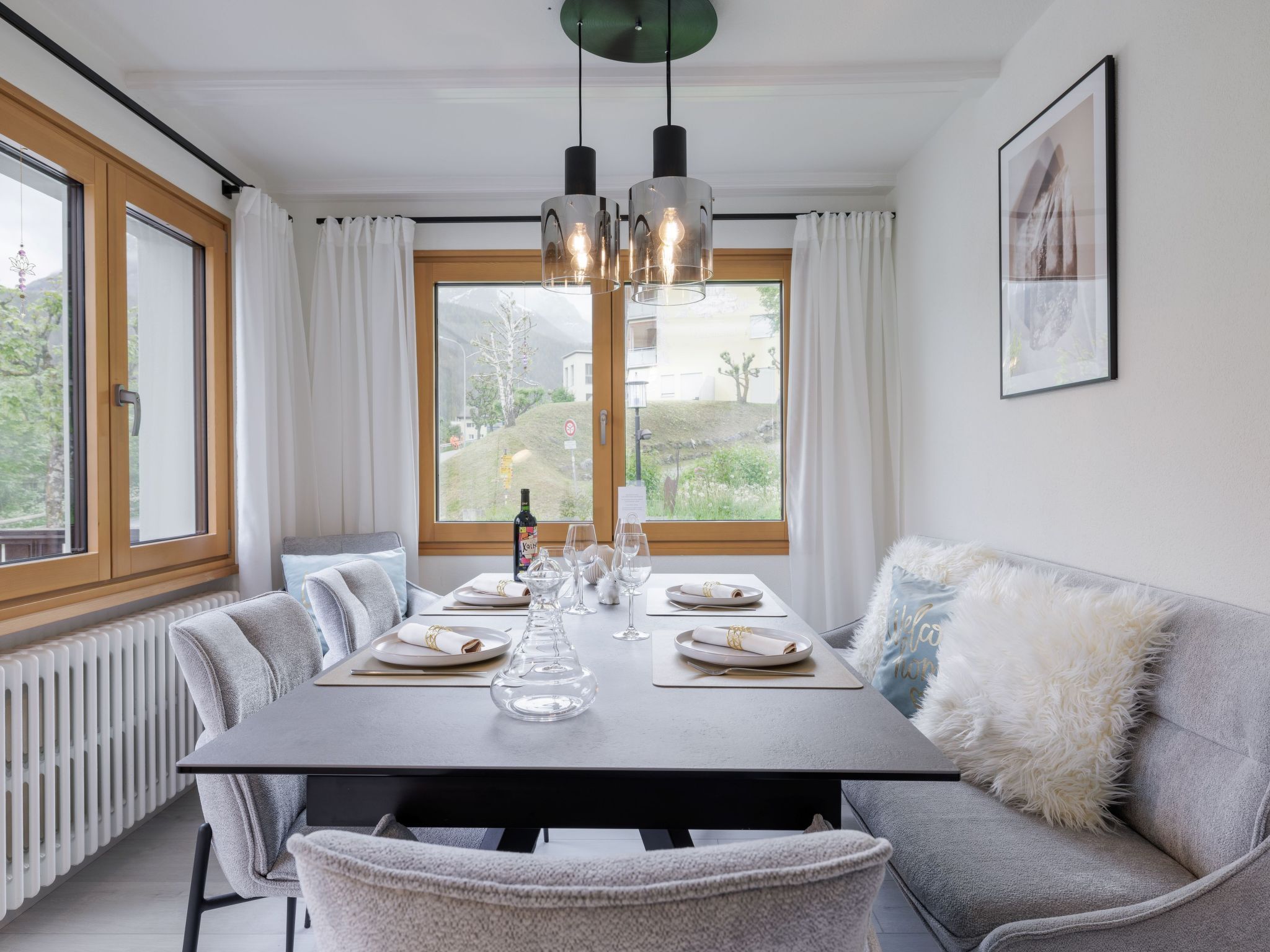A dining area with a table set for four, two pendant lights, a radiator, and a window with curtains.