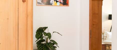 A hallway with a wooden cabinet, a woven basket with a plant, and a colorful abstract painting on the wall.