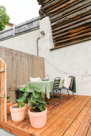 An outdoor patio with a wooden deck, a table set with plates and glasses, two potted plants, and a chair with a green cover. - Chasa Savü, (Guarda) by Interhome (Guarda)