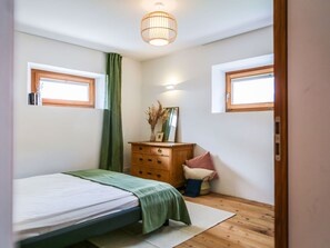 A bedroom with a bed, a dresser, a mirror, and two windows. - Chasa Savü, (Guarda) by Interhome (Guarda)