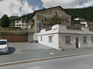 Ein zweistöckiges Gebäude mit Balkon, Parkplatz und Blick auf die Berge.