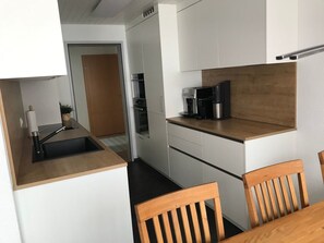 Eine moderne Küche mit weißen Schränken, einer Holzausziehtafel, einer Kaffeemaschine und einem Spülbecken.