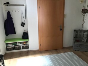 Ein Zimmer mit einer Holztür, einem Kleiderständer mit einer Jacke, einer kleinen schwarzen Tasche und einer grünen Bank mit Stauraumkörben.