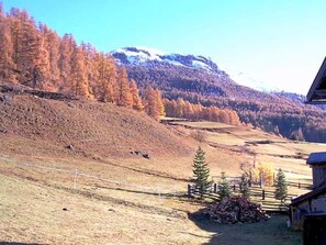 Un paisaje rural con una cabaña de madera, una pila de leña y una vista despejada de una cordillera.