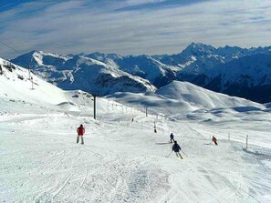 Una pista de esquí nevada con esquiadores, un telesilla y montañas al fondo.