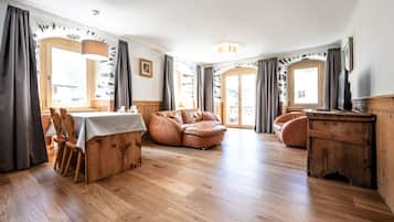 Ein großzügiger Wohnbereich mit Holzboden, Ledersofas, einem Esstisch mit Stühlen und großen, mit Vorhängen versehenen Fenstern.