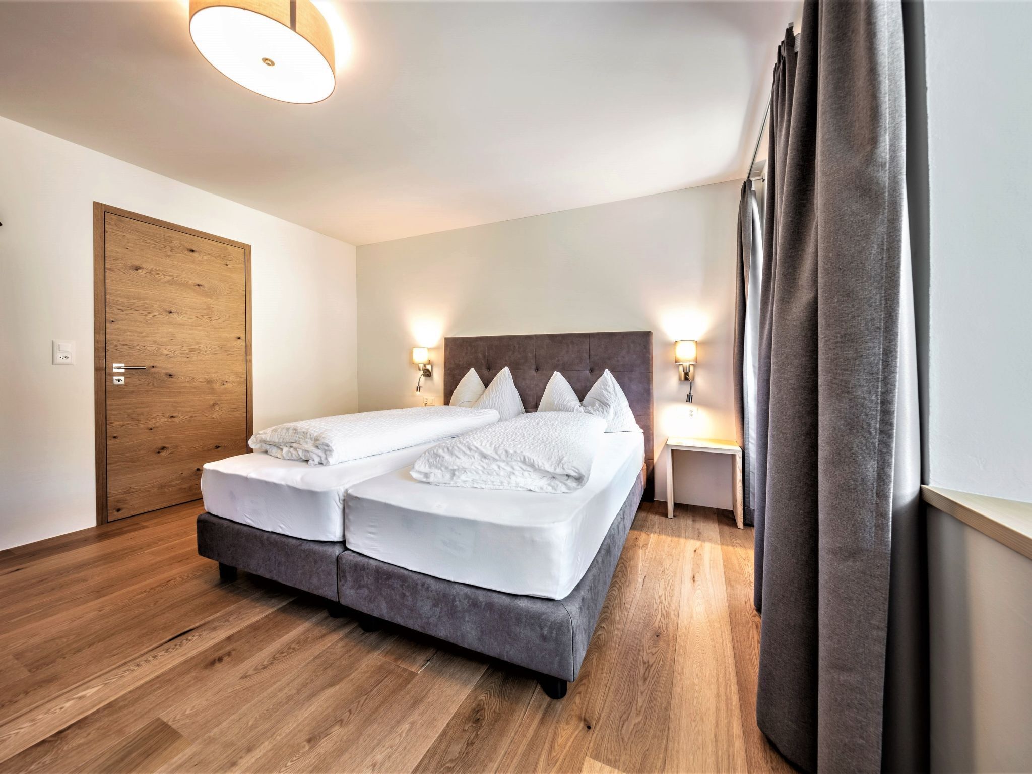 Ein Doppelbett mit Kopfteil, zwei Nachttische mit Lampen, ein Holzschrank und ein Vorhang.