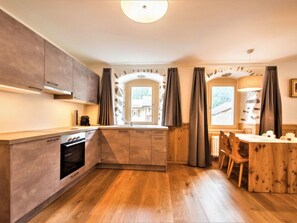 Une cuisine moderne avec des meubles en bois, un four encastré et un coin repas comprenant une table et des chaises en bois.