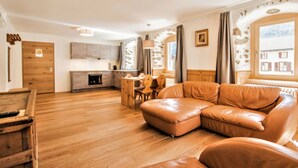 Un salon moderne avec un plancher en bois, un canapé en cuir, un coin repas et une cuisine aux murs en pierre.