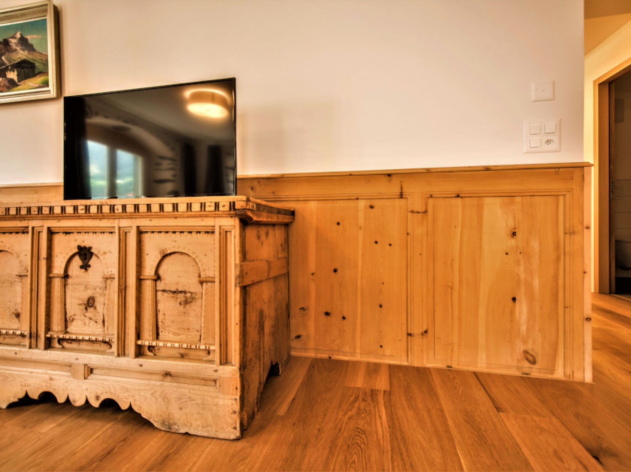 Ein Holzkabinett mit einem Fernseher darauf, ein gerahmtes Bild an der Wand und ein Holzboden.