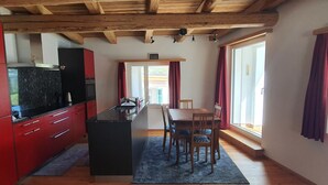 Una cocina con armarios rojos, encimera negra y zona de comedor de madera con una mesa y sillas.