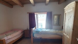 Un dormitorio pequeño y acogedor con dos camas individuales, un armario de madera, una ventana con cortinas y un espejo en la pared.