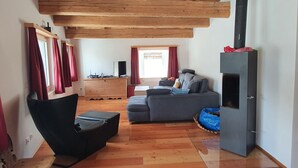 Un salón acogedor con techo de madera, un sofá gris, un sillón negro y una chimenea.