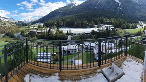 Un paisaje montañoso con un río, edificios y una terraza de madera.