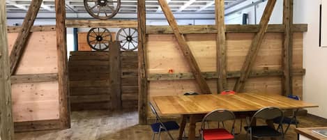 A rustic wooden interior with a high ceiling, exposed beams, and a wooden table with chairs.