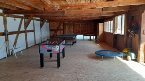 Ein Innenbereich mit Holzbalken, einem Kicker, einer Hüpfburg und einem Tischtennistisch.