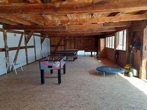 An indoor space with wooden beams, a foosball table, a trampoline, and a window with a view.