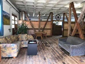 Ein rustikales Blockhaus-Interieur mit Holzbalken, einem Holztisch, zwei Sofas und einem großen Fenster.