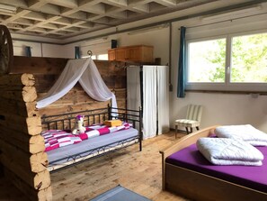 A rustic room with a wooden bunk bed, a separate bed with a purple mattress, a chair, and a window with curtains. - Ferienwohnungen Paclerahof, (Sta. Maria - Santa Maria Val Müstair) by Interhome (Sta. Maria GR)