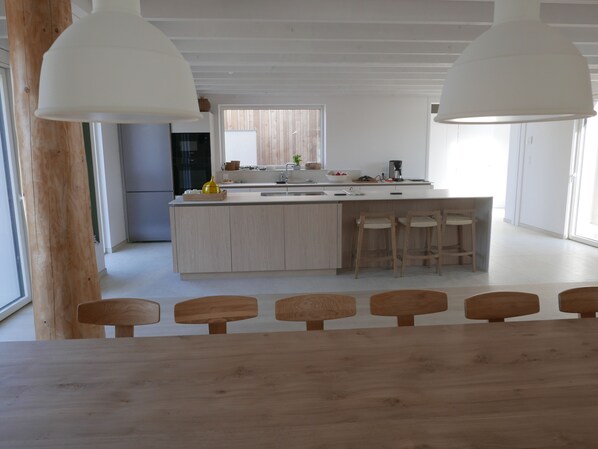 Une cuisine moderne dotée d’un îlot central, de chaises en bois et de luminaires suspendus.