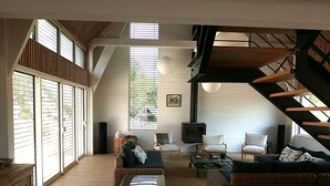 A spacious living area with large windows, a fireplace, and a staircase.