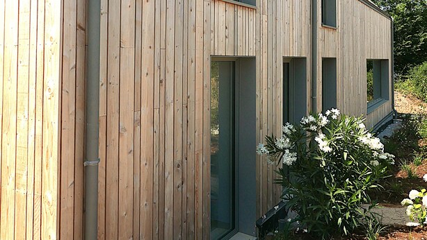 A modern wooden building with multiple windows and a visible gutter system.