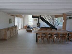 Una habitación amplia con zona de comedor, sofá, escalera y un gran ventanal.