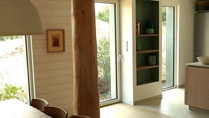 A dining area with a wooden table and chairs, a large wooden beam, and a view through a glass door to an outdoor area.