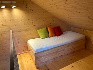 Un lit superposé en bois avec un matelas et des oreillers, un plancher en bois et un plafond en pente avec un luminaire.