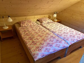 Une chambre dans une cabane en bois, avec deux lits, chacun recouvert d’une courtepointe à motifs, deux lampes de chevet et un plancher en bois.