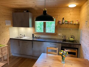 Une cuisine compacte avec une fenêtre, des placards en bois, un évier et un coin repas agrémenté d’un vase de fleurs.