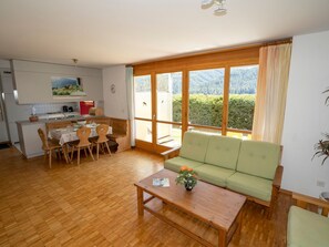 A spacious living area with a wooden floor, a green sofa, a dining table with chairs, and a kitchen in the background. - Senda, (Scuol) by Interhome (Scuol)