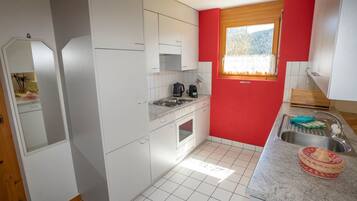 A compact kitchen with white cabinets, a built-in oven, a sink, and a window with a view of trees.