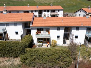 A multi-story residential building with a red-tiled roof, balconies, and a front patio with outdoor seating. - Senda, (Scuol) by Interhome (Scuol)