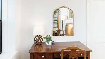 Una scrivania in legno con una lampada, una sedia e uno specchio in una stanza con pavimento in legno e pareti bianche.
