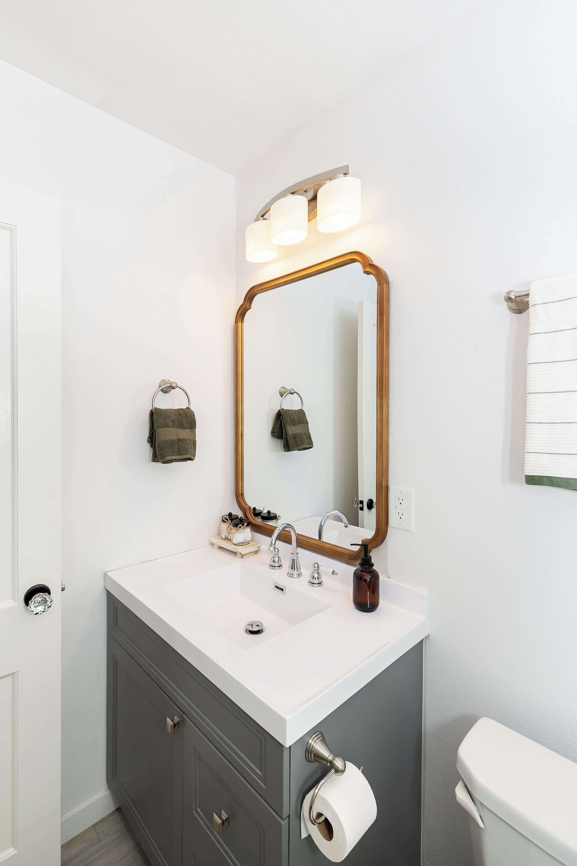 A bathroom with a white sink, a mirror with a wooden frame, a towel rack, and a toilet.