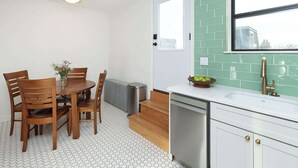 Una cocina con encimera blanca, un lavamanos, una ventana y un comedor con sillas y mesa.
