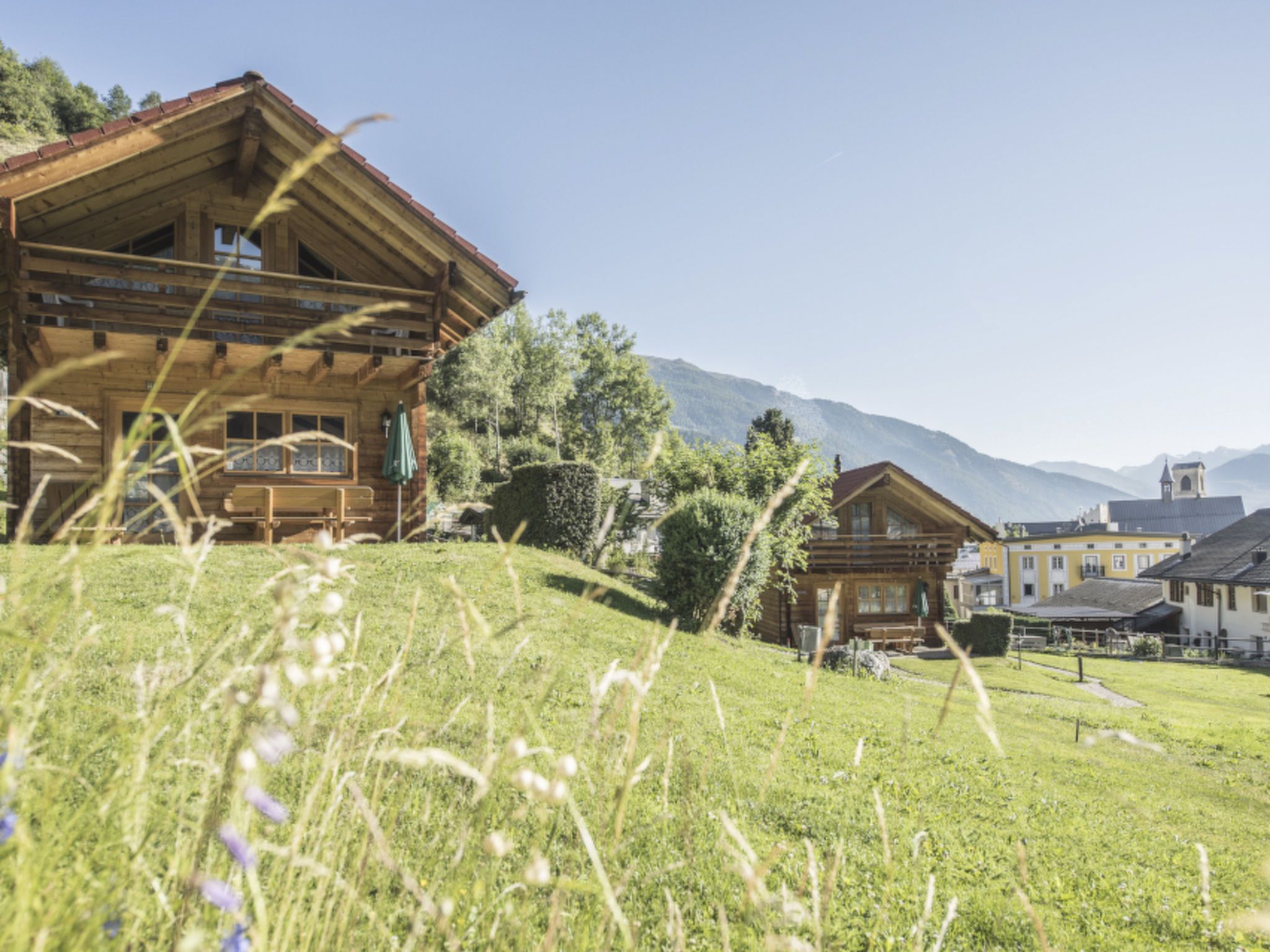 A wooden chalet with a sloped roof, surrounded by a grassy hillside and trees.