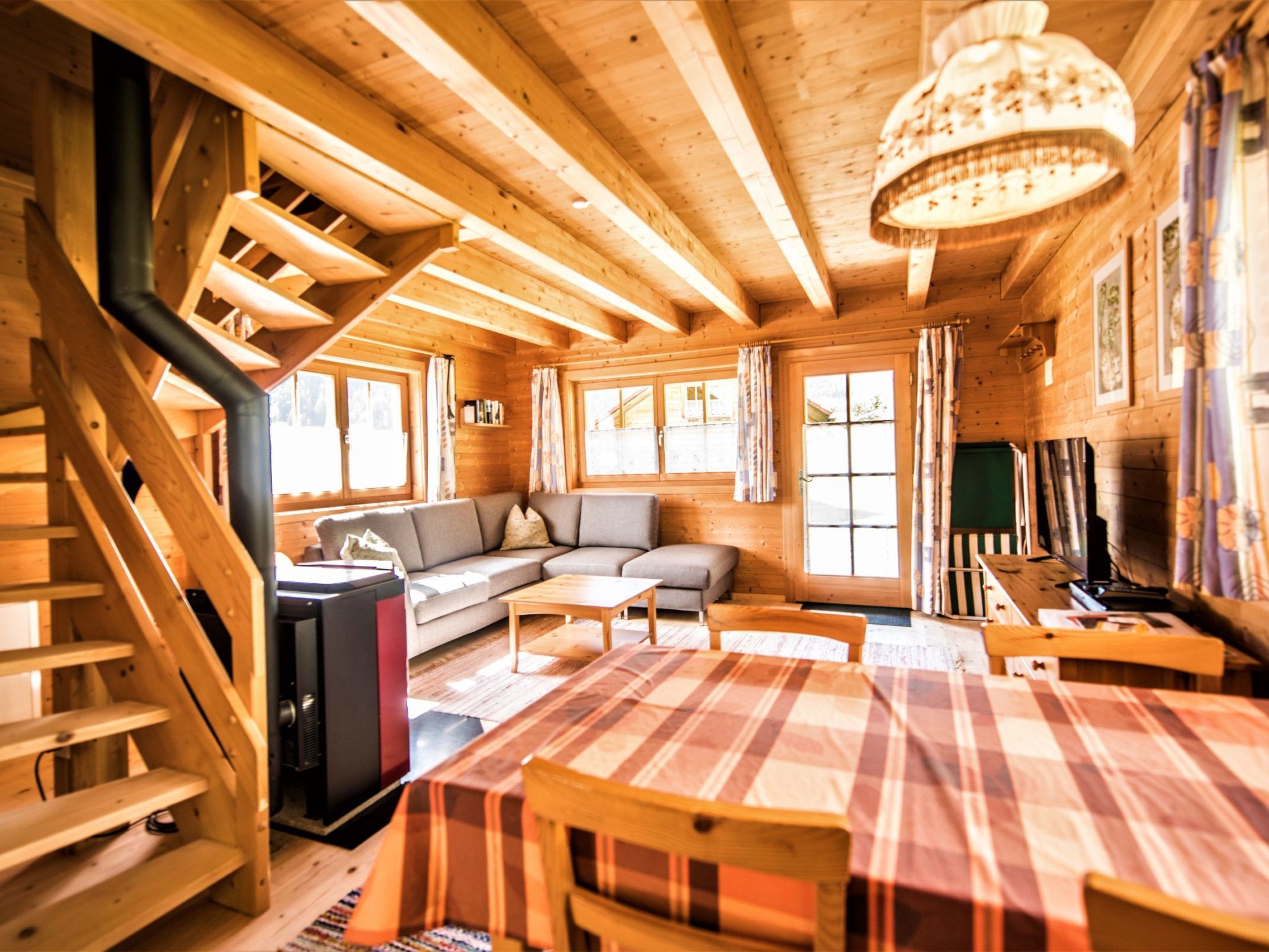 Interior de una cabaña de madera con escalera, sofá, mesa de comedor y televisor.