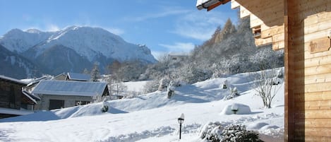 Un paisaje montañoso nevado con construcciones de madera, cielo despejado y un sendero cubierto de nieve.