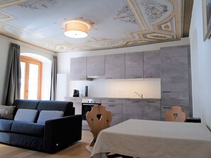 Een moderne keuken met grijze kastjes, een eettafel met een witte tafelkleed en een bank met kussens.