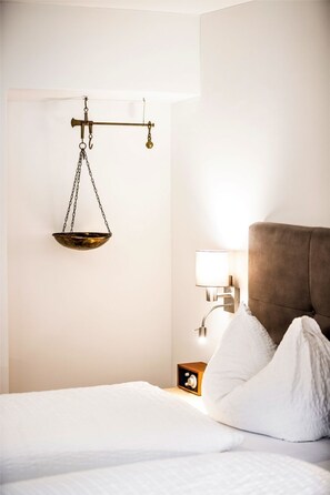 Une chambre d’hôtel avec un lit, du linge de lit blanc, une balance, une lampe de chevet et une table de chevet avec une horloge.